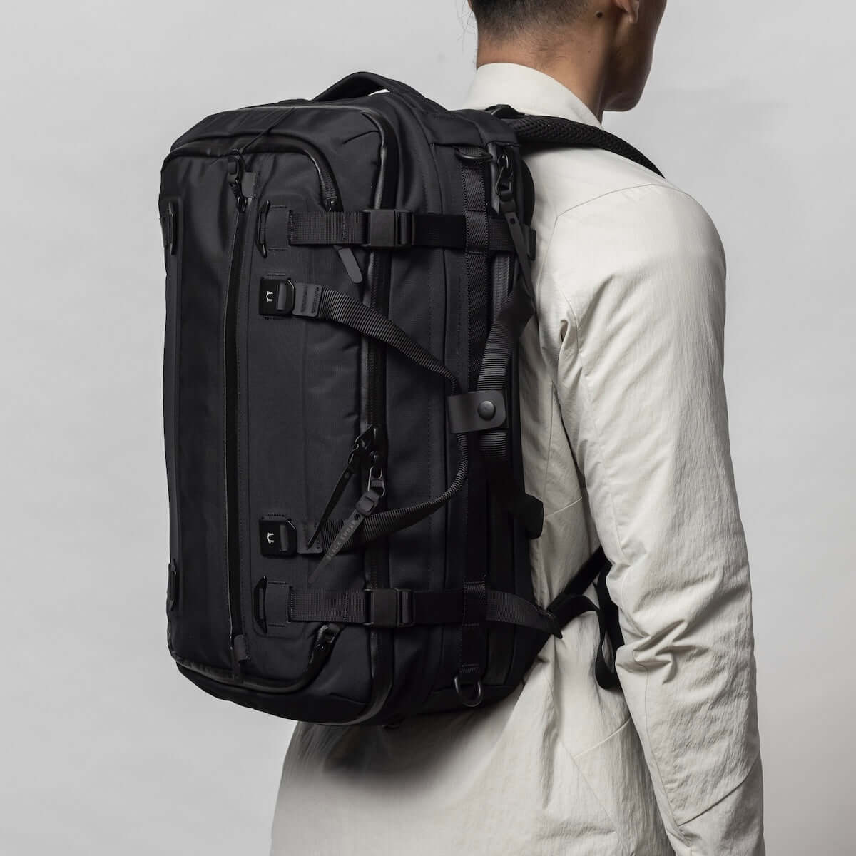 Black Ember FORGE 40L travel backpack shown from the side on a model, illustrating its expandable design and versatile carrying options.