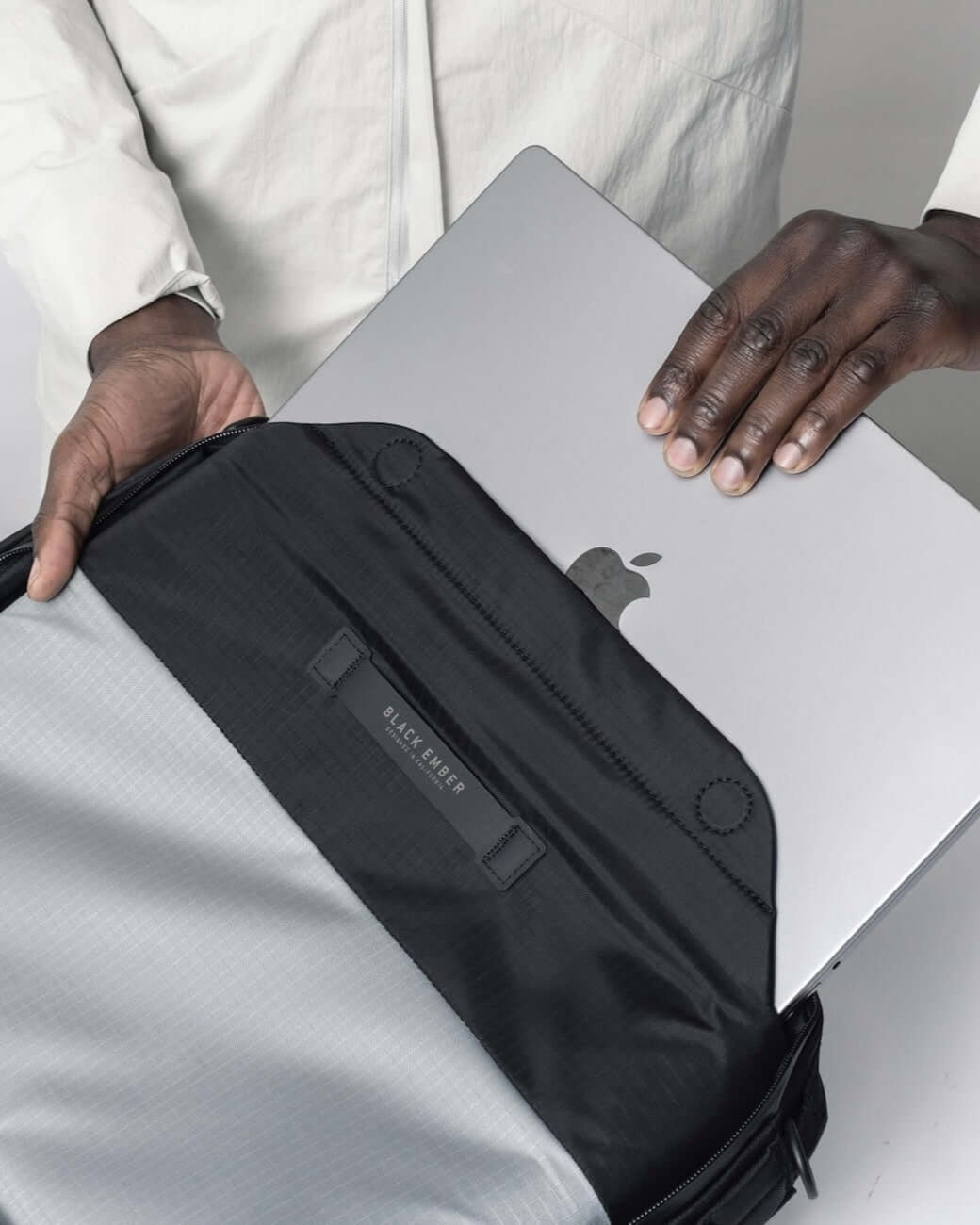 Black Ember FORGE SB 20L minimalist soft brief with padded laptop compartment, shown holding a MacBook for everyday carry convenience.