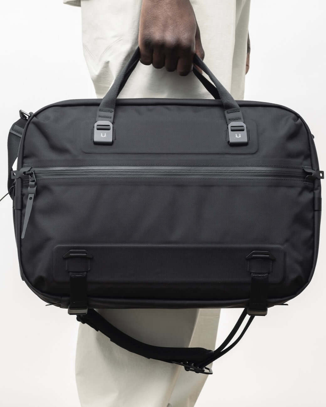 Black Ember FORGE SB 20L minimalist soft brief in black, shown carried by hand with top handles, ideal for EDC and business travel.