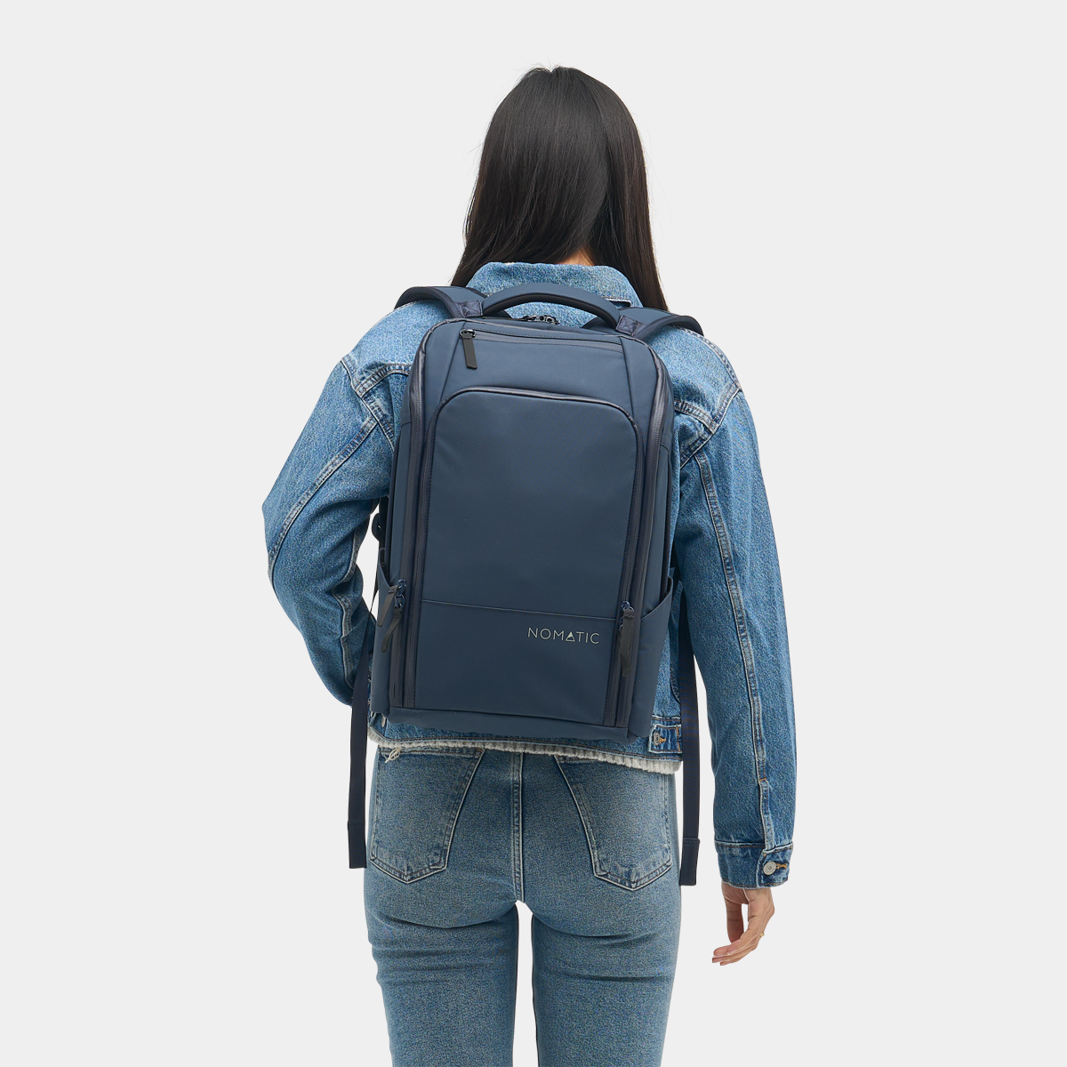 Nomatic Travel Pack in navy blue worn by a woman, showcasing its sleek design, expandable storage, and weather-resistant material.