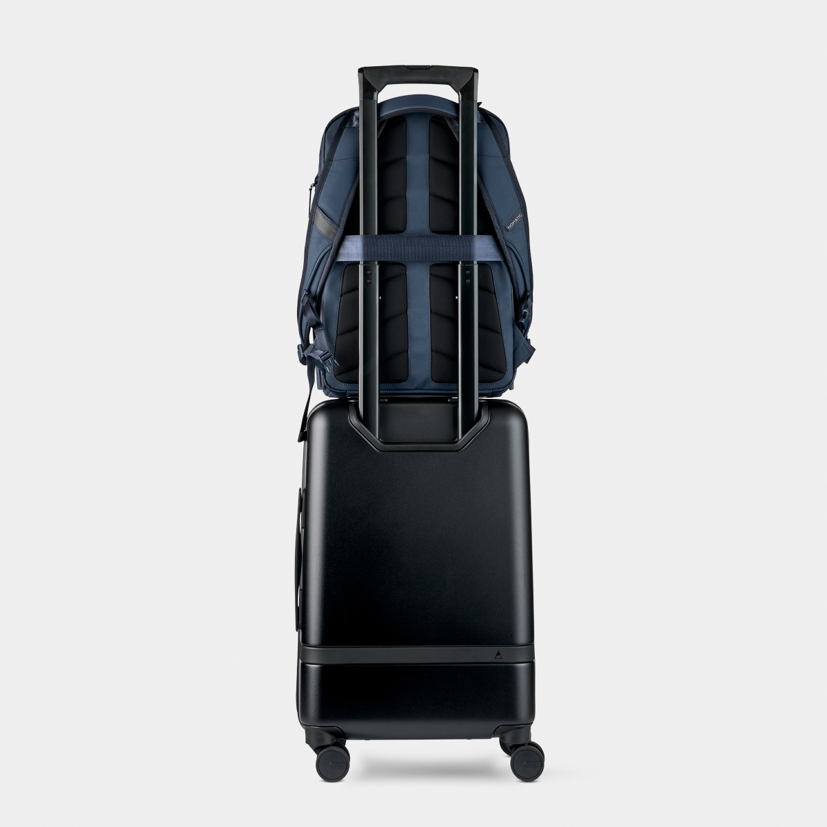 Nomatic Travel Pack in navy blue securely attached to a black rolling suitcase handle, showcasing its luggage pass-through sleeve for easy travel.
