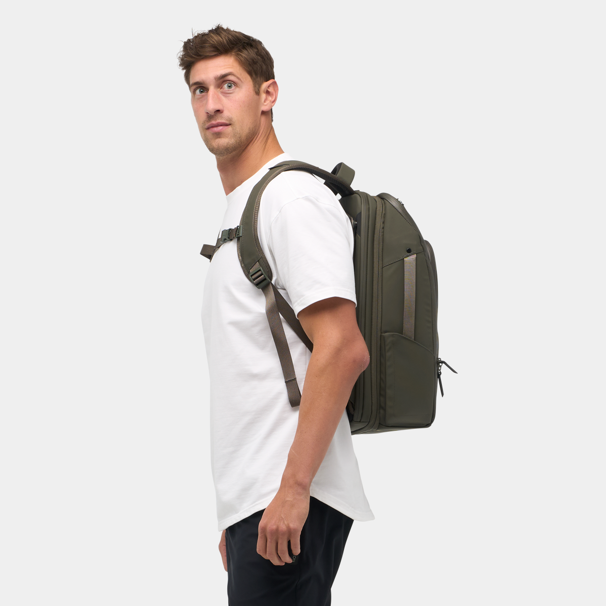 Man wearing the Nomatic Travel Pack in olive green, showcasing its expandable design and sleek laptop backpack profile for travel organization.